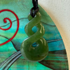 Green jade spiral pendant on a textured surface with abstract designs